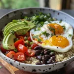 A close-up view of a colorful breakfast bowl featuring quinoa, eggs, avocado, black beans, and tomatoes.