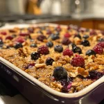 A close-up side view of a warm berry oatmeal bake topped with fresh berries.