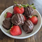 Close-up view of chocolate-covered strawberry truffles with a glossy finish.