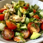 A close-up view of a vibrant avocado chicken salad with diced avocados, cooked chicken, cherry tomatoes, and cucumber.