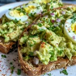 Close-up of Avocado Egg Salad Toast topped with fresh herbs.