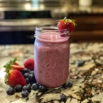 A close-up side view of a berry avocado smoothie in a glass.