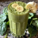 Close-up of a creamy green smoothie filled with banana and spinach, served in a glass.