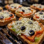 Close-up view of mini garlic toast pizzas topped with tomato sauce, cheese, bell pepper, and black olives.