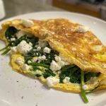 Close-up view of a fluffy Spinach and Feta Omelette garnished with fresh spinach.
