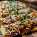 Close-up view of BBQ Chicken Flatbread topped with shredded cheese and honey drizzle.