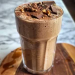 Close-up view of a chocolate peanut butter banana smoothie in a glass, topped with a banana slice.