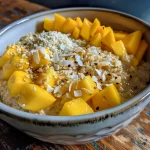 Close-up view of creamy coconut mango oatmeal topped with fresh mango and toasted coconut.