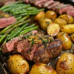Close-up view of a Herbed Steak Sheet Pan Dinner with juicy steak, halved baby potatoes, and green beans.