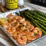 Close-up view of juicy lemon garlic shrimp and asparagus on a sheet pan.