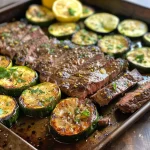 Juicy sliced sirloin steak alongside lemon zucchini on a sheet pan.