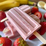 Side view of vibrant strawberry banana protein popsicles on a wooden table.