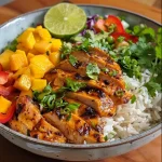 Close-up view of a bowl filled with Mango Chili Lime Chicken, coconut rice, and colorful toppings.