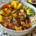 A vibrant bowl featuring grilled chicken, pineapple, and colorful bell peppers on a bed of coconut rice.