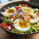 A close-up view of a bowl containing quartered hard boiled eggs and chopped avocado, garnished with red onion and red bell pepper.