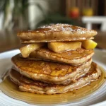 Close-up view of golden brown apple cinnamon pancakes stacked on a plate.