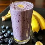 Close-up of a Blueberry Banana Protein Smoothie in a glass, featuring vibrant blueberries and banana slices.