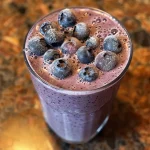 A close-up view of a creamy blueberry vanilla almond smoothie in a glass.