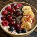 A close-up side view of a bowl of Cherry Berry Banana Overnight Oats topped with fresh cherries and berries.