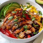 Close-up view of a colorful chicken fajita rice bowl with sliced chicken, bell peppers, and avocado.
