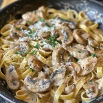 A plate of creamy mushroom pasta with sliced chicken, garnished with parsley.