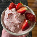 A close-up side view of creamy homemade strawberry yogurt in a bowl, topped with fresh strawberries.