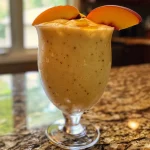 Close-up view of a peach yogurt smoothie in a glass with a peach slice garnish.