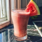 Close-up side view of a vibrant watermelon protein shake in a glass with ice.