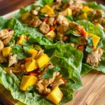 ['Close-up view of Chicken Mango Lettuce Wraps featuring vibrant ingredients.', 'Juicy Chicken Mango Lettuce Wraps displayed with colorful vegetables and herbs.', 'Side view of fresh Chicken Mango Lettuce Wraps on a wooden platter.', 'Delicious Chicken Mango Lettuce Wraps arranged attractively with toppings.']