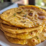 ['A close-up of a golden-brown chickpea flatbread on a wooden surface.', 'Side view of a fluffy chickpea flatbread, showcasing its texture and color.', 'A freshly cooked chickpea flatbread with a slight sheen, highlighting its oiliness.', 'A vibrant image of chickpea flatbread, emphasizing the crispy edges and soft center.']