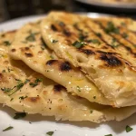 ['Close-up view of a golden-brown gluten-free flatbread on a wooden surface.', 'Side view of a soft, textured gluten-free flatbread, showcasing its layers.', 'Detailed image of a gluten-free flatbread with a slightly crispy edge on a plate.', 'Juicy gluten-free flatbread displayed with a rustic background.']