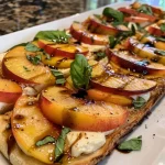 ['Close-up side view of Peach Caprese Flatbread with fresh ingredients.', 'Sliced Peach Caprese Flatbread featuring mozzarella and basil.', 'Juicy peach slices on flatbread, surrounded by mozzarella and balsamic glaze.', 'Flatbread topped with peaches, mozzarella, and basil, captured from the side.']