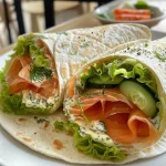 ['Close-up view of a smoked salmon wrap filled with cream cheese, cucumber, and herbs.', 'Side angle of a delicious smoked salmon wrap showcasing its vibrant ingredients.', 'Detailed photo of a smoked salmon and herbed cream cheese wrap with colorful fillings.', 'Close-up of a fresh smoked salmon wrap with visible layers of cream cheese and vegetables.']