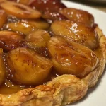 ['A close-up side view of a slice of apple tarte Tatin topped with vanilla ice cream and apple purée.', 'A delicious slice of apple tarte Tatin with a scoop of vanilla ice cream beside it on a plate.', 'An appetizing side view of apple tarte Tatin served with a generous dollop of vanilla ice cream and drizzled with apple purée.', 'A visually appealing slice of apple tarte Tatin displaying caramelized apples and accompanied by creamy vanilla ice cream.']
