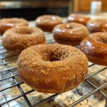 ['Close-up of a Baked Apple Cider Donut with a glaze, showcasing a soft texture.', 'Side view of a Baked Apple Cider Donut, revealing its moist interior and cinnamon topping.', 'A golden Baked Apple Cider Donut placed on a rustic wooden surface, highlighting its deliciousness.', 'A freshly baked Apple Cider Donut, with a sprinkle of cinnamon sugar on top.']