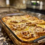['Close-up side view of a baked cinnamon roll casserole with a golden-brown top.', 'A delicious cinnamon roll casserole, showing gooey cinnamon rolls and a creamy texture.', 'Cinnamon roll casserole displayed from the side, highlighting its fluffy layers and icing drizzle.', 'Close-up image of a cinnamon roll casserole, featuring swirls of cinnamon and frosting on top.']