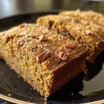 ['A side view of a gluten-free pumpkin cake topped with pecan crumble, showcasing its moist texture.', 'Close-up of a gluten-free pumpkin cake, highlighting the orange zest and pecan topping.', 'Detailed side view of a pumpkin cake with a crunchy pecan crumble, emphasizing its rich color.', 'Juicy gluten-free pumpkin cake with a golden-brown pecan topping captured from the side.']