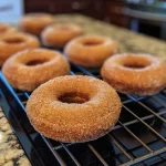 ['Close-up of a healthy baked apple cider donut with a golden-brown exterior.', 'Side view of a soft, moist baked apple cider donut sprinkled with cinnamon.', 'Juicy, delicious apple cider donut on a white plate, showcasing its texture.', 'Appetizing healthy baked donut with a glossy finish, highlighting cinnamon topping.']