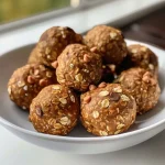 ['Close-up of No Bake Pumpkin Spice Energy Bites on a wooden surface.', 'Side view of delicious, round pumpkin spice energy bites with chocolate chips.', 'Smooth, textured No Bake Pumpkin Spice Energy Bites displayed in a cozy setting.', 'Hand holding a pumpkin spice energy bite with a blurred background.']