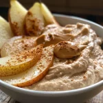 ['Close-up of a juicy pear sliced and served with peanut butter yogurt dip.', 'Side view of fresh pear slices accompanied by a creamy peanut butter dip.', 'A small bowl of peanut butter yogurt dip next to pear slices on a plate.', 'Juicy pear wedges displayed with a dollop of peanut butter yogurt dip.']
