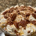['Close-up view of creamy pecan pie dip in a serving bowl.', 'Side angle of a delicious pecan pie dip with chopped pecans on top.', 'Creamy dessert dip showcasing a rich mix of pecans and cream cheese.', 'Tasty pecan pie dip displayed in a bowl, highlighting its creamy texture.']