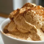 ['A close-up side view of creamy Protein Pumpkin Fluff in a bowl.', 'Delicious Protein Pumpkin Fluff with a smooth texture, served in a white bowl.', 'Side view of Protein Pumpkin Fluff, highlighting its rich and creamy appearance.', 'Close-up image of a bowl filled with Protein Pumpkin Fluff, showing its vibrant orange color.']