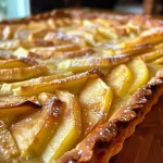 ['Close-up side view of a rustic apple tart with golden crust and visible apple slices.', 'Detailed shot of a delicious apple tart showing the flaky crust and juicy apple filling.', 'Side view of a freshly baked rustic apple tart highlighting its texture and layered apples.', 'Juicy rustic apple tart presented on a plate, featuring a golden-brown crust and apple slices.']