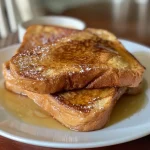 ['Close-up of juicy Sourdough French Toast topped with syrup.', 'Side view of a stack of golden Sourdough French Toast on a plate.', 'A delicious plate of Sourdough French Toast with syrup drizzled on top.', 'Sourdough French Toast slices with a sprinkle of cinnamon.']