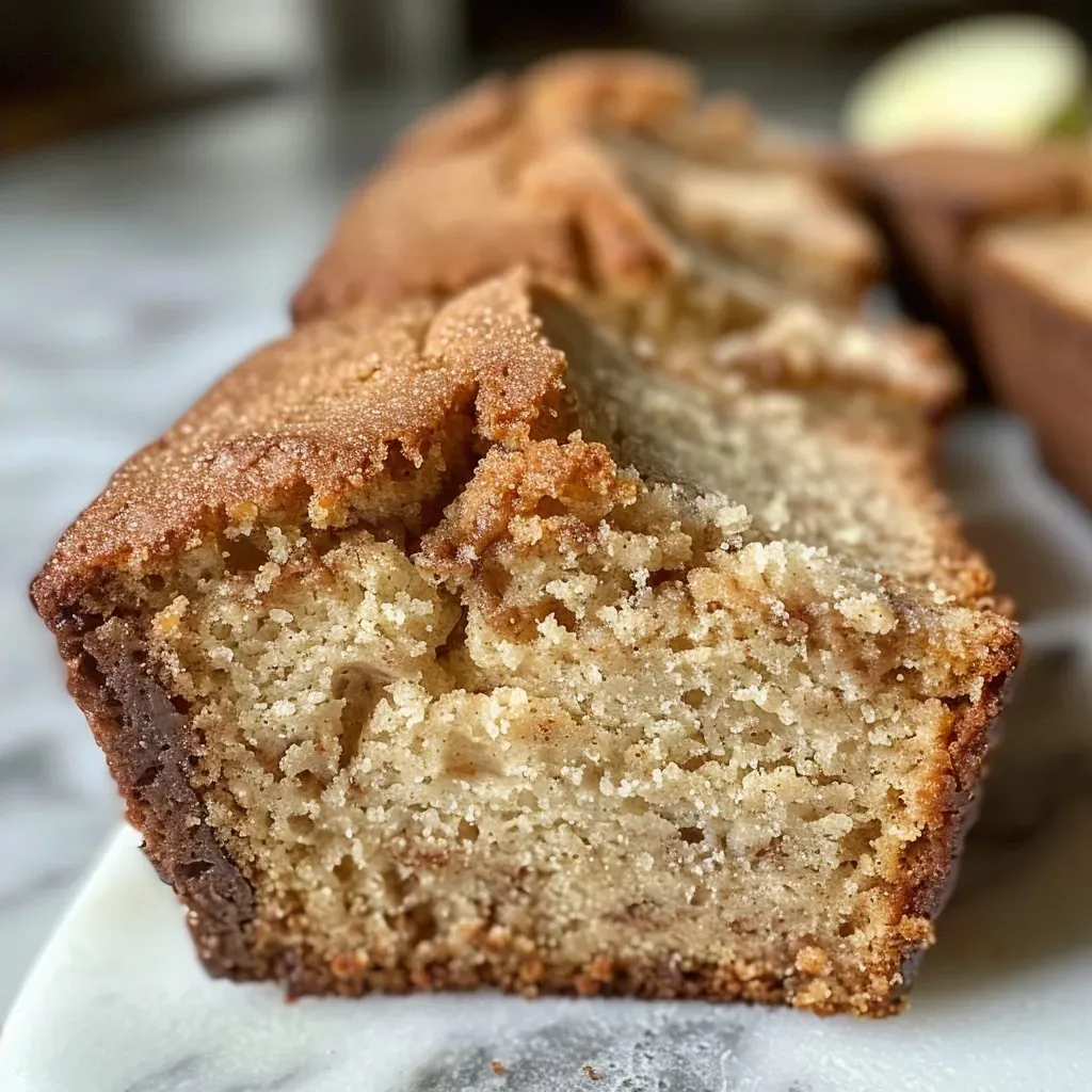 ['Close-up view of a moist Apple Cider Donut Bread showcasing a golden-brown crust.', 'Side angle of freshly baked Apple Cider Donut Bread with a crumbly texture.', 'Detailed view of a slice of Apple Cider Donut Bread highlighting its juicy interior.', 'Close-up image of Apple Cider Donut Bread with visible sugar coating and spice aroma.']