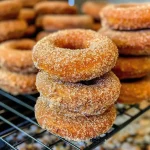 ['Golden brown baked apple cider donuts arranged on a plate.', 'Close-up view of a delicious baked apple cider donut, showcasing its texture.', 'A stack of freshly baked apple cider donuts with a light cinnamon sugar coating.', 'Side view of moist baked apple cider donuts with a glossy glaze.']