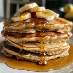 ['Close-up of fluffy brown butter banana pancakes topped with toasted pecans.', 'Side view of delicious banana pancakes with a drizzle of syrup and crunchy pecans.', 'Brown butter banana pancakes garnished with chopped pecans and a soft, golden-brown exterior.', 'Juicy, stacked banana pancakes with a rich brown glaze and pecans scattered on top.']