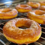 ['Close-up of a golden, glazed butternut squash donut with a smooth texture.', 'Side view of fluffy butternut squash donuts dusted with powdered sugar.', 'A delicious butternut squash donut showcasing its rich color and soft appearance.', 'Deliciously plump butternut squash donut with a light coating of sugar.']