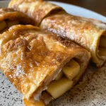 ['Close-up view of Cinnamon Apple Protein Rollups on a plate, showcasing a golden-brown exterior.', 'Side view of rolled protein snacks filled with apple pieces and cinnamon, resting on a wooden table.', 'Delicious Cinnamon Apple Protein Rollups presented on a rustic surface, highlighting their texture.', 'Juicy protein rollups filled with apple and cinnamon, captured in natural light for a appetizing look.']
