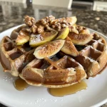 ['Close-up of golden-brown waffles topped with figs and walnuts.', 'Side view of fluffy waffles showcasing a sprinkle of cinnamon and chopped walnuts.', 'Delicious waffles garnished with sliced figs and a drizzle of syrup.', 'Irresistible stack of waffles with visible texture and toppings of walnuts and figs.']